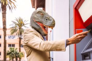 man wearing a dinosaur head at an ATM