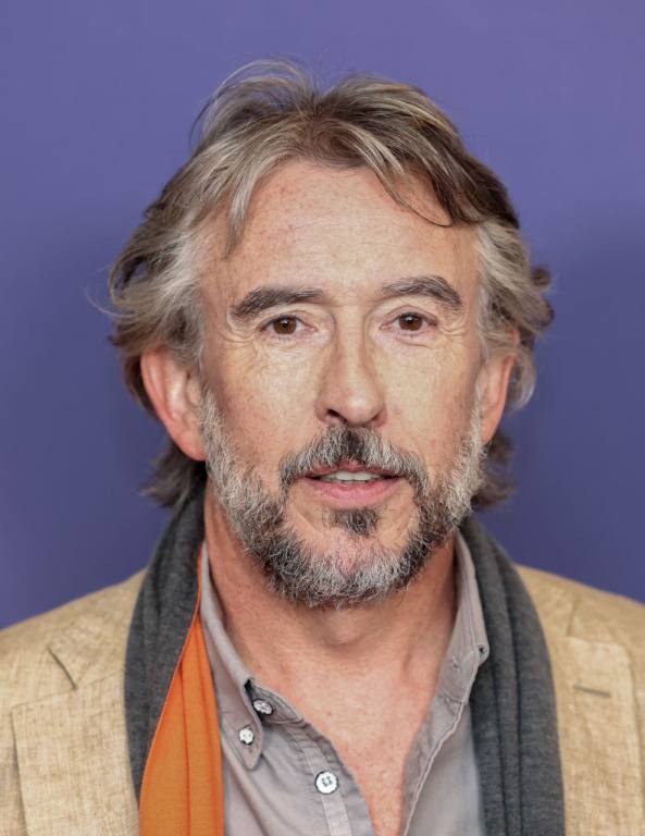 Steve Coogan attends the UK premiere of "The Lost King." He has a beard, grayish hard and is wearing a beige blazer.