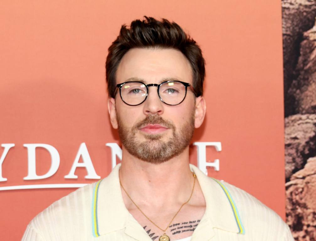 Chris Evans attends the Apple Original Films' "Ghosted" New York Premiere wearing black frame glasses and a cream-colored collared shirt with green trim.