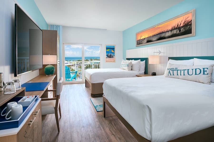 Two queen sized beds in white covers with a view of the ocean out of a sliding glass door. Margaritaville Introductory Rates