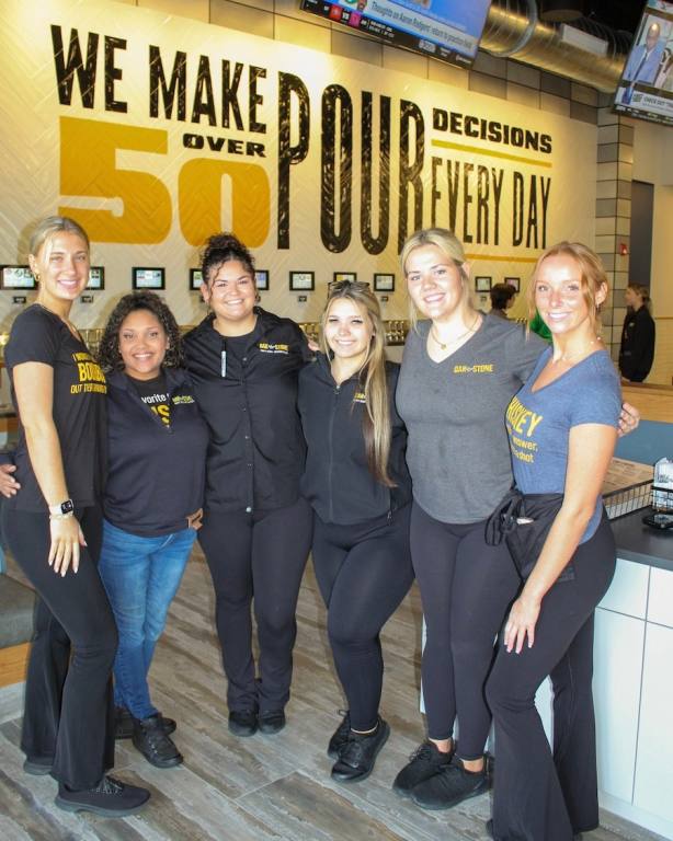 six smiling ladies in front of a wall full of beer taps