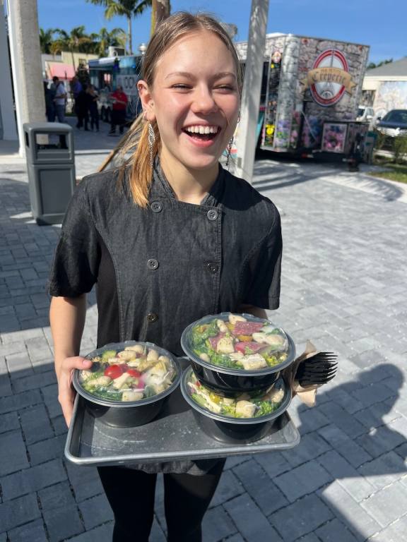 A smilng girl holding a tray of salads