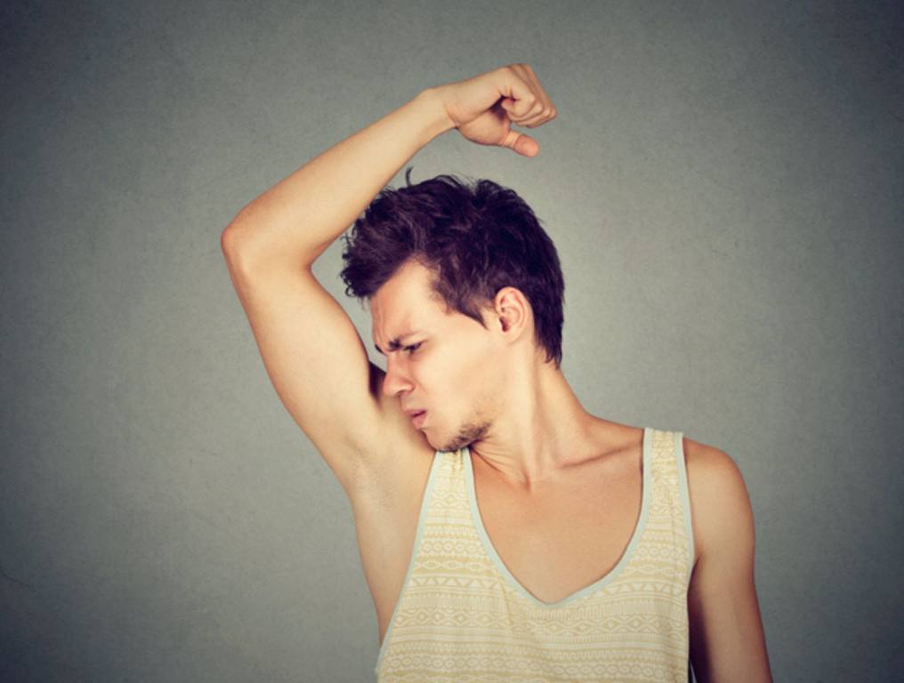 Closeup portrait of young man, smelling, sniffing his armpit, something stinks, very bad, foul odor situation, isolated on gray wall background. Negative emotion, facial expression, feeling.