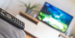 TV remote control in the foreground, tv in the blurry background. Streaming.