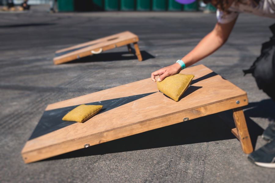 Cornhole board with bean bags and a hand reaching for one