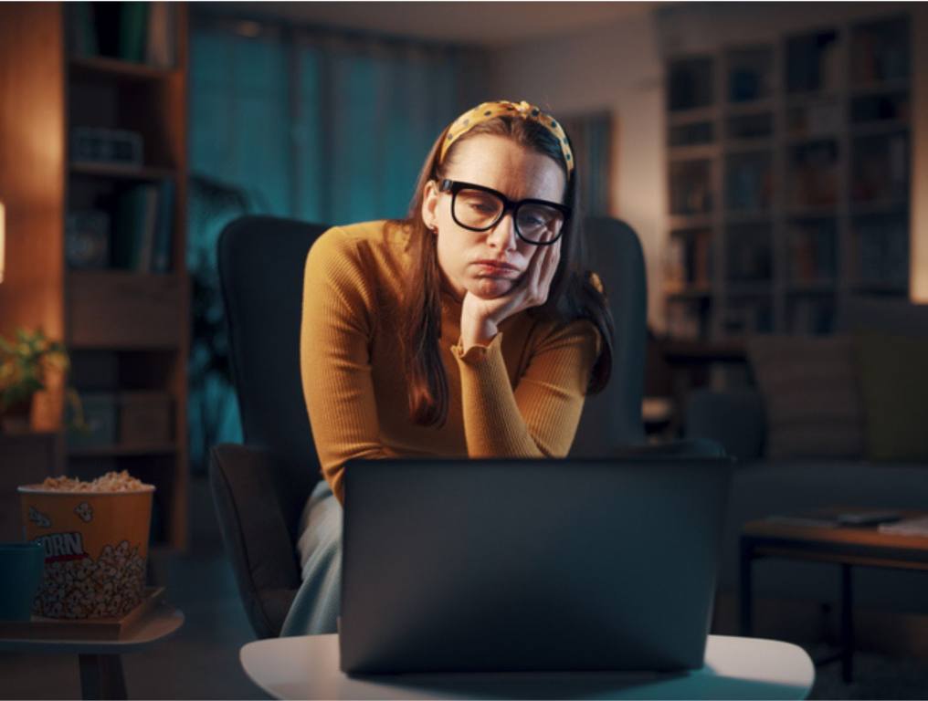 Bored sad woman sitting in the living room at home and connecting with her laptop