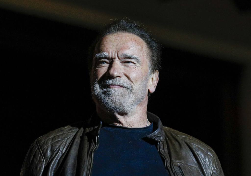 Arnold Schwarzenegger speaks during Netflix's Tudum: A Global Fan Event 2023 smiling looking left with a leather jacket, Arnold Schwarzenegger Has A Pacemaker After 3 Surgeries.