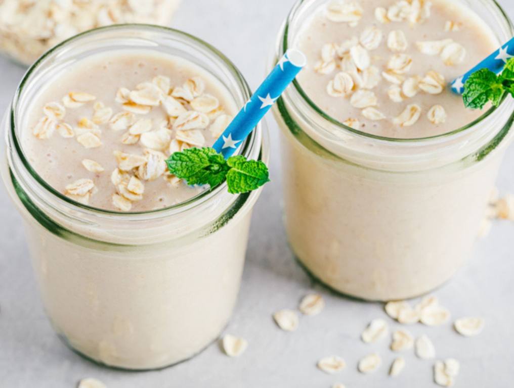 Banana oats smoothie or milkshake in glass mason jars on a stone background