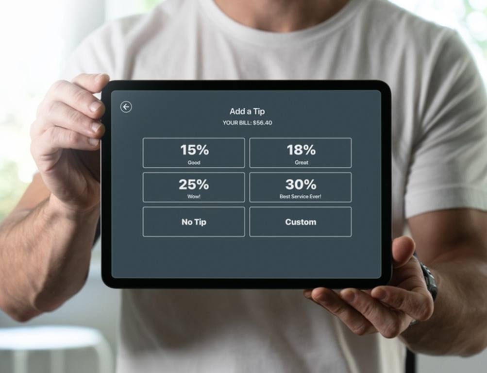 Man holding a tablet with tipping screen inside a restaurant