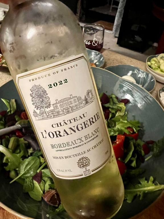 Bottle ofChateau L'Orangerie Bordeaux Blanc with a salad in the background