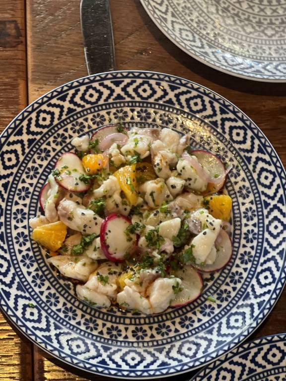 Blue and white plate with chunks of white fish, herbs and a lemon wedges