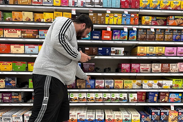 Man wearing grey sweat shirt looks for items on grocery store shelf.