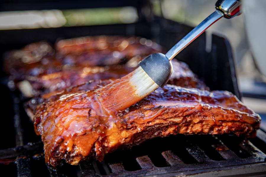 slab of ribs on a grill, being basted with BBQ sauce