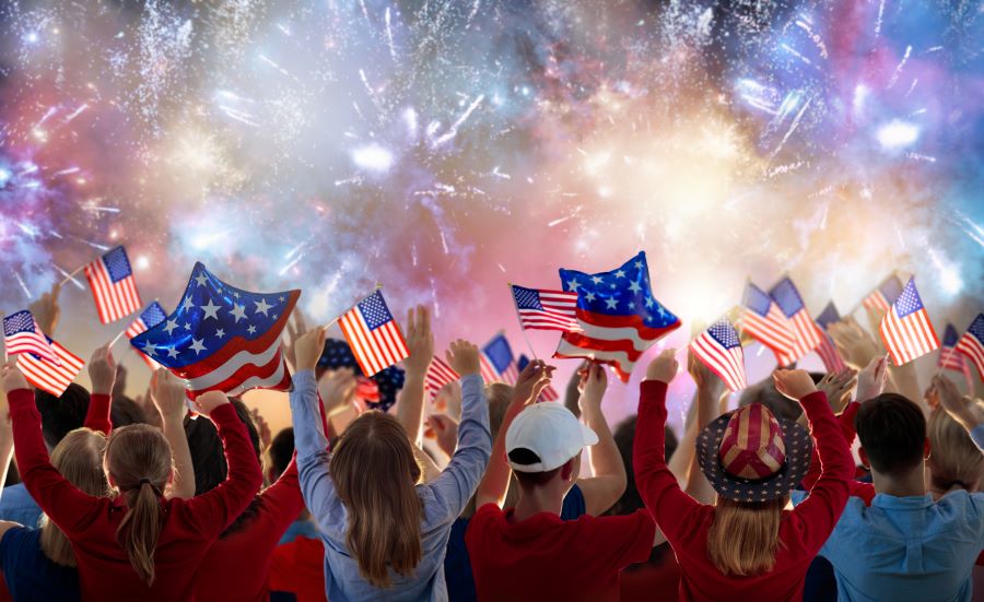 Fireworks in the sky, people on ground with red white and blue flags and stars