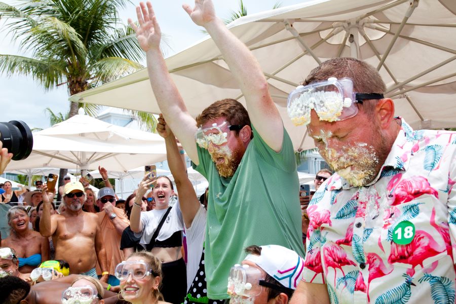 Two men with pie all over their face. One has his hands in the air as in victory