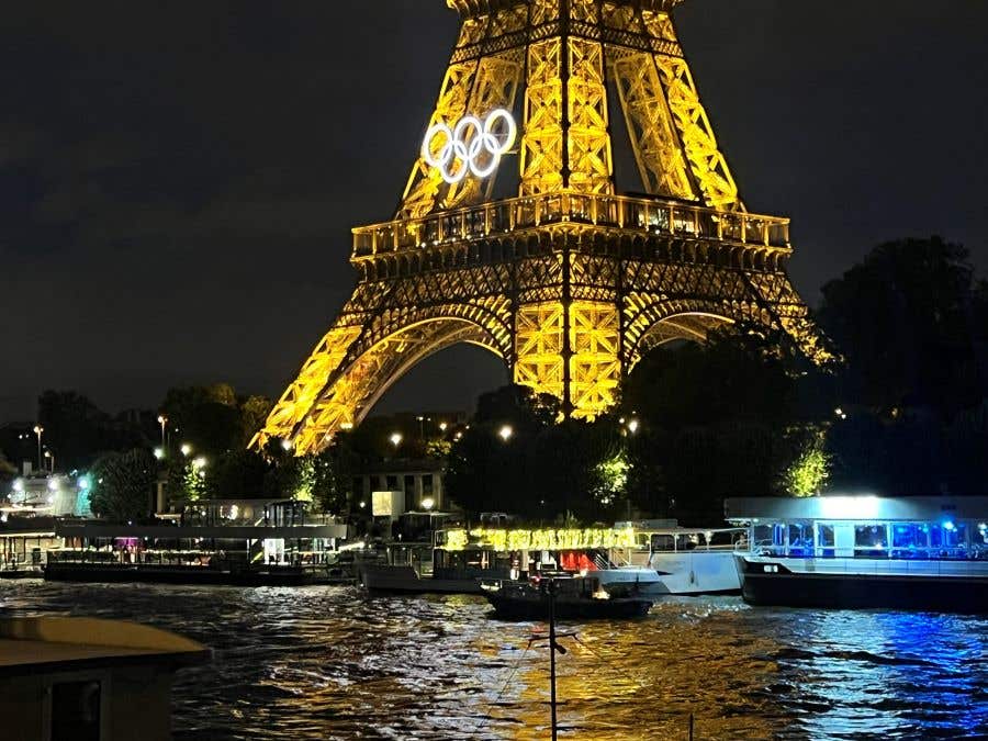 Eiffel Tower lit up at night with the Olympic Rings on the front, behind the River Seine