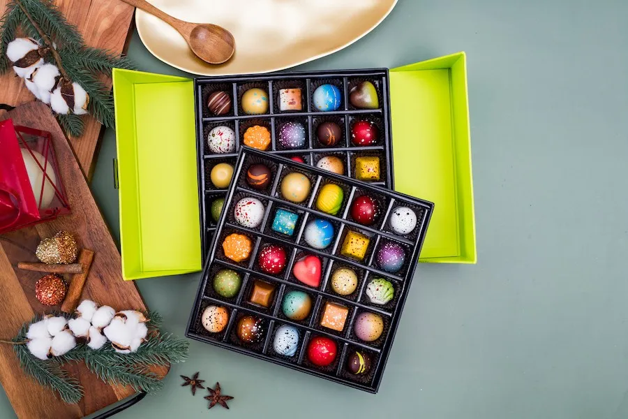 Box of colorful round chocolates with Christmas decor in the background. Christmas In July With Norman Love Chocolates