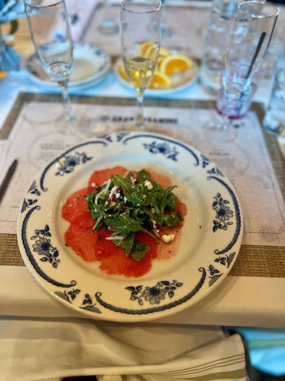 White plate with thinly sliced pieces of watermelon and arugula in the middle