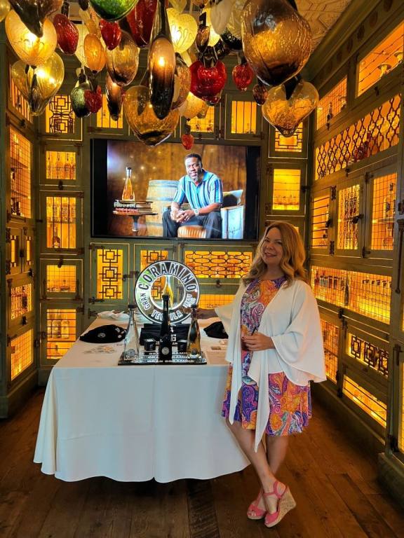 A woman in a colorful dress standing next to three bottles of Grran Coramino Tequila