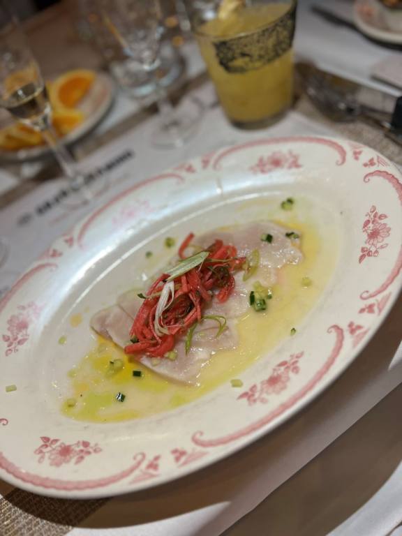 Round plate with thin pieces of wahoo fish topped with shreds of red, pickled watermelon radish