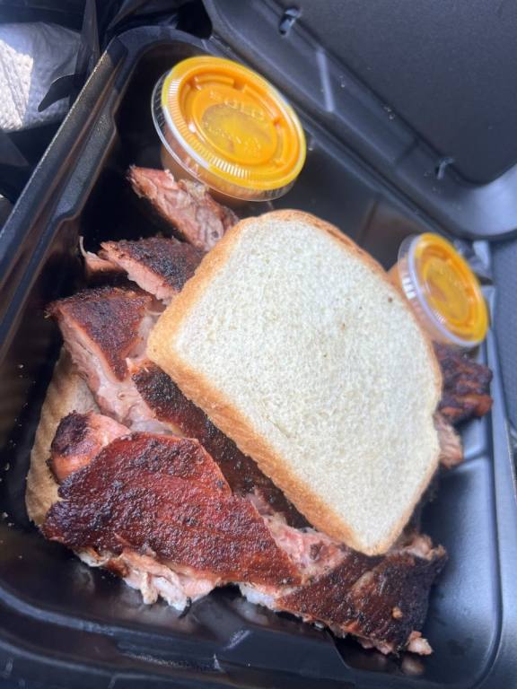 White bread with slabs of BBQ meat in the middle, sauce in small containers on the side