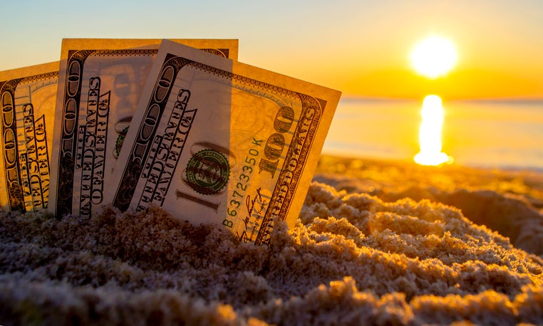 Three dollar bills are buried in sand on sandy beach near sea at sunset dawn in summer close-up.