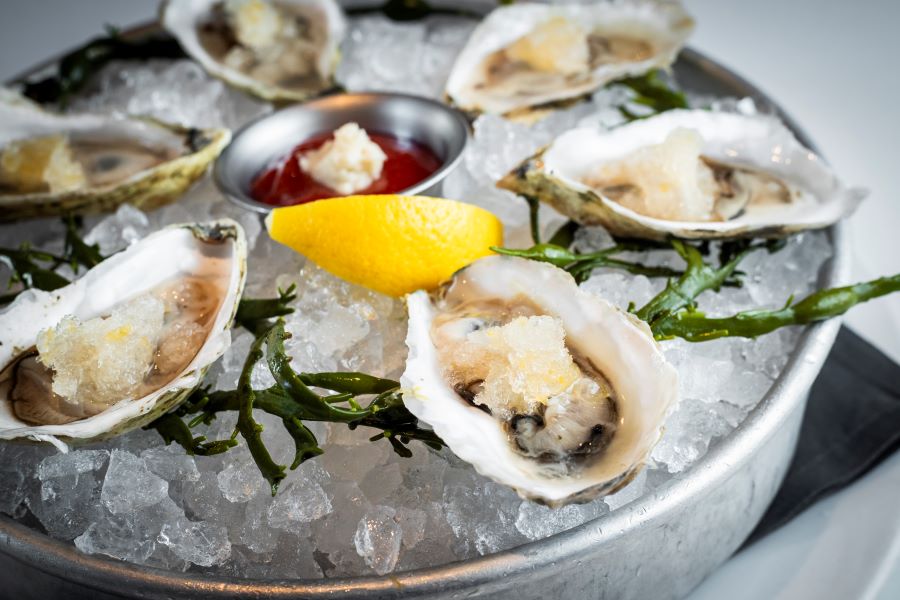 Round tray full of ice and raw oysters in the half shell with a wedge of lemon, Oyster Specials In Downtown Naples