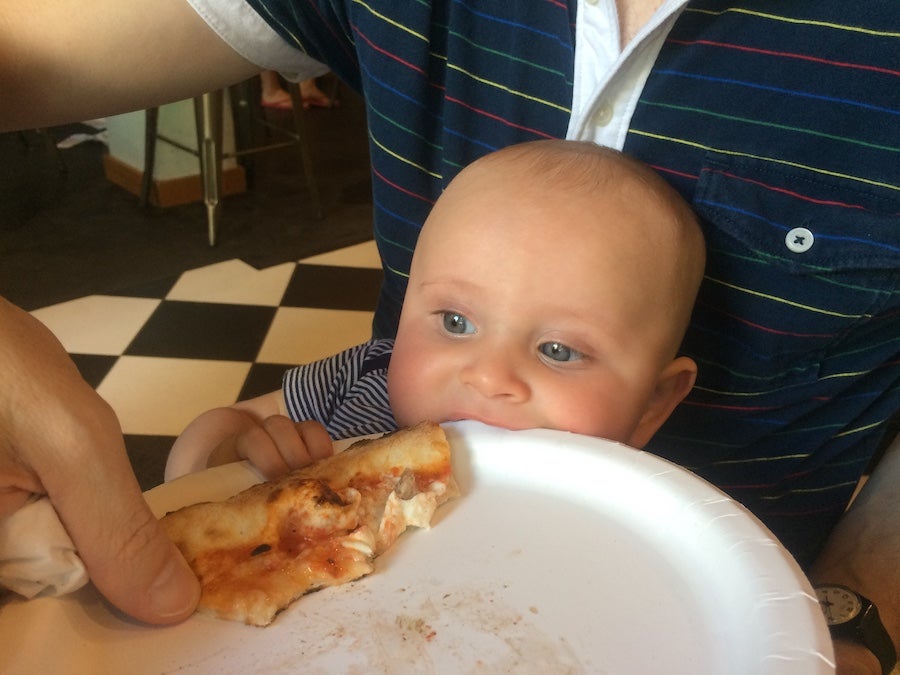 Baby peering over the edige of a plate with a large slice of pizza part of fun baby videos