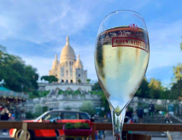 Champagne glass filled to the top in the foreground. Background is the grand Sacre Coeur in Paris. Olympic Worthy Wines to sip this summer