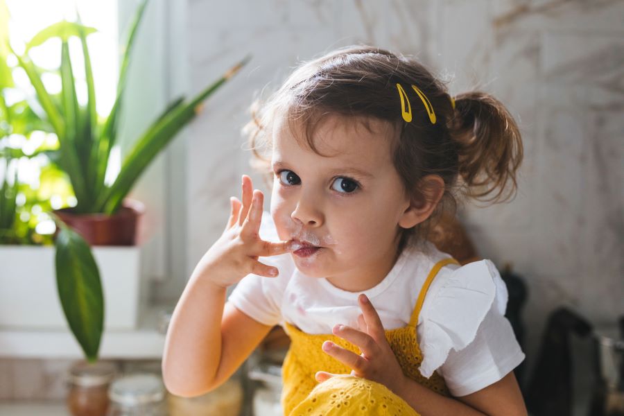 Little girl at a table licking her fingers for kids eat free for back to school