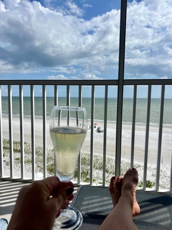 View of beach from a a balcony with a railing. A woman's hand holding up a glass of Champagne.