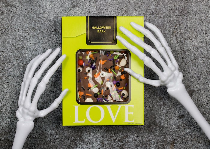 box of Norman Love chocolate being held by fake skelton hands for Norman Love Halloween Chocolates