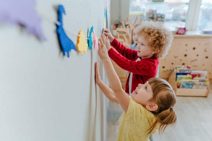 Preschool students playing in kindergarten with color dinosaur figures on the wall. Selective focus.