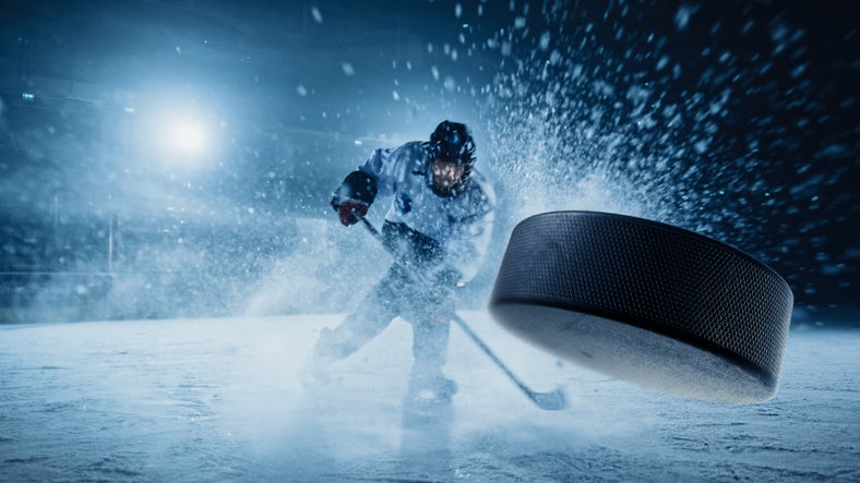 Ice Hockey Rink Arena: Professional Player Shooting the Puck with Hockey Stick. Focus on 3D Flying Puck with Blur Motion Effect. Dramatic Wide Shot, Cinematic Lighting. for SWFL Holiday Events