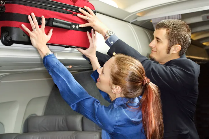 Couple putting suitcase in overhead for compartment New Flights And Big Sales From RSW